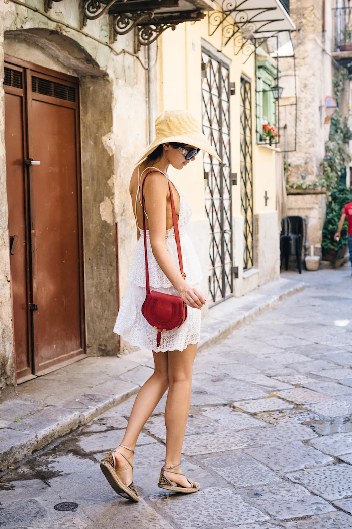 brunette woman wearing short white boho lace dress cute outfit ideas sandals and hat red bag and sunglasses