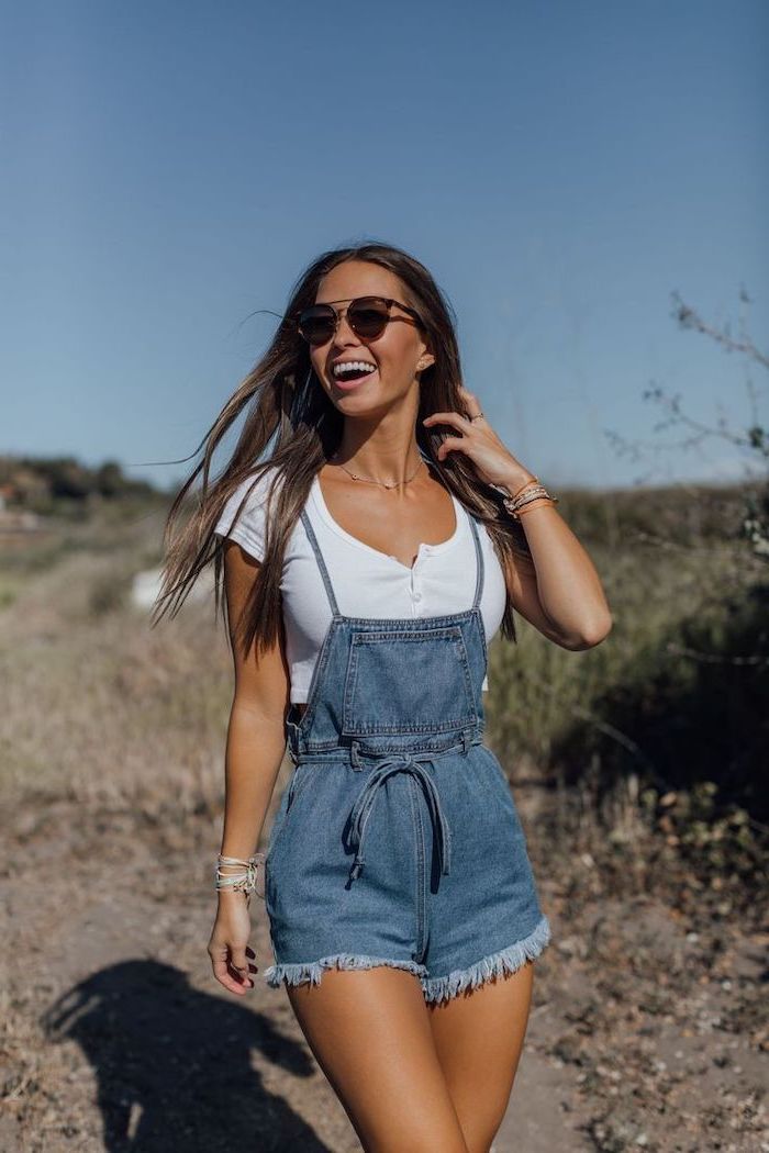 brunette woman wearing sunglasses denim jumpsuit with white crop top summer outfit ideas lots of small bracelets