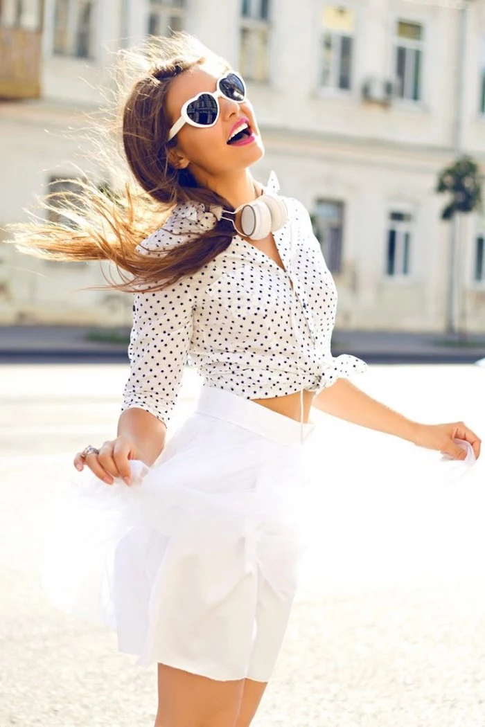 brunette woman wearing white skirt white shirt with black dots tied at the front cute trendy outfits heart shaped white sunglasses