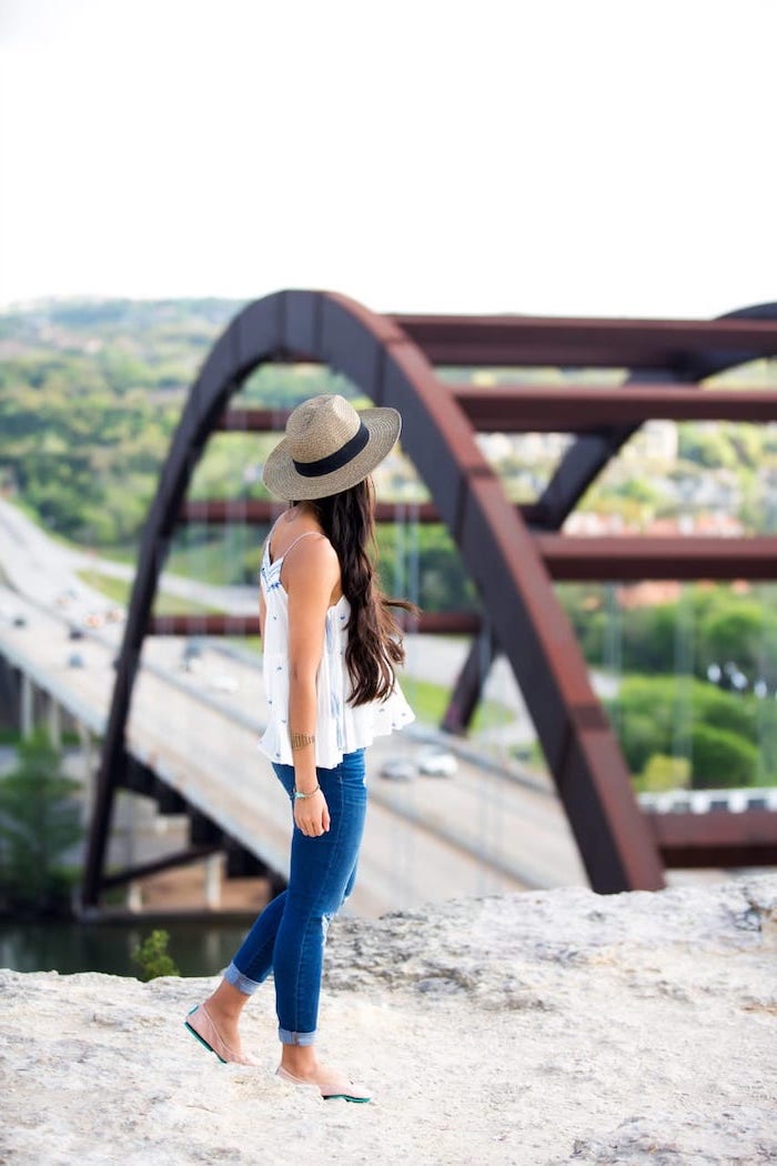 cute trendy outfits woman with long brown wavy hair wearing jeans white top hat standing on rock