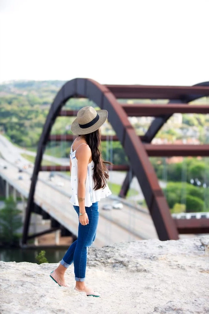 cute trendy outfits woman with long brown wavy hair wearing jeans white top hat standing on rock
