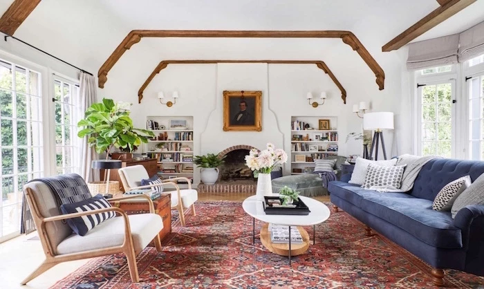 blue velvet sofa, two white armchairs, farmhouse living room ideas, colorful carpet, exposed wooden beams on white ceiling