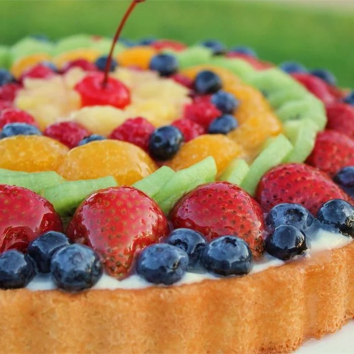 fruit cake with blueberries strawberries kiwi orange raspberries pineapple arranged in circles on top cherry in the middle easy no bake desserts
