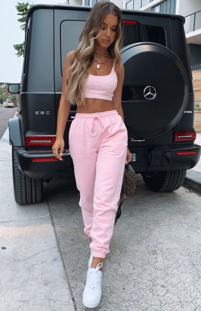 girl with long blonde wavy hair cute summer clothes wearing pink sweatpants and crop top with white sneakers