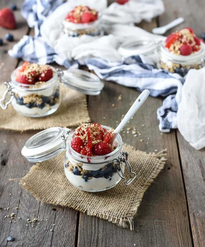 glass jars filled with cheesecake parfaits no bake dessert recipes made with blueberries strawberries and oatmeal