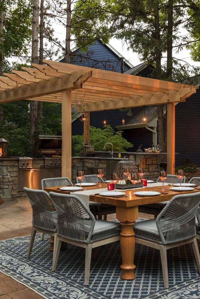 grey chairs around wooden table on grey carpet outdoor cooking station made of stone with grill cabinets sink