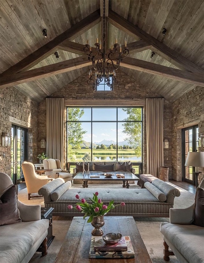 farmhouse style homes, wooden ceiling with exposed beams, grey furniture set, tall windows, stone walls