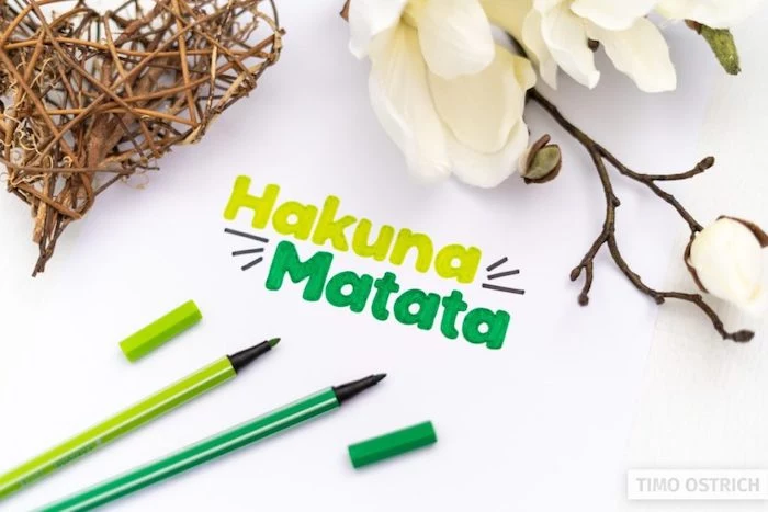 hakuna matata written in different shades of green hand lettering white background with white flowers