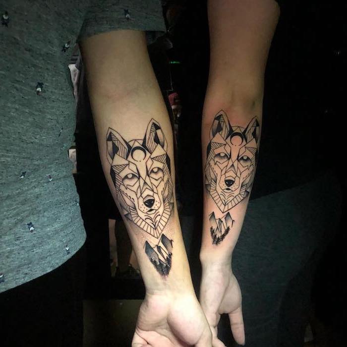matching tattoos on the back of the arm twin tattoos geometric wolf heads with mountain landscape underneath