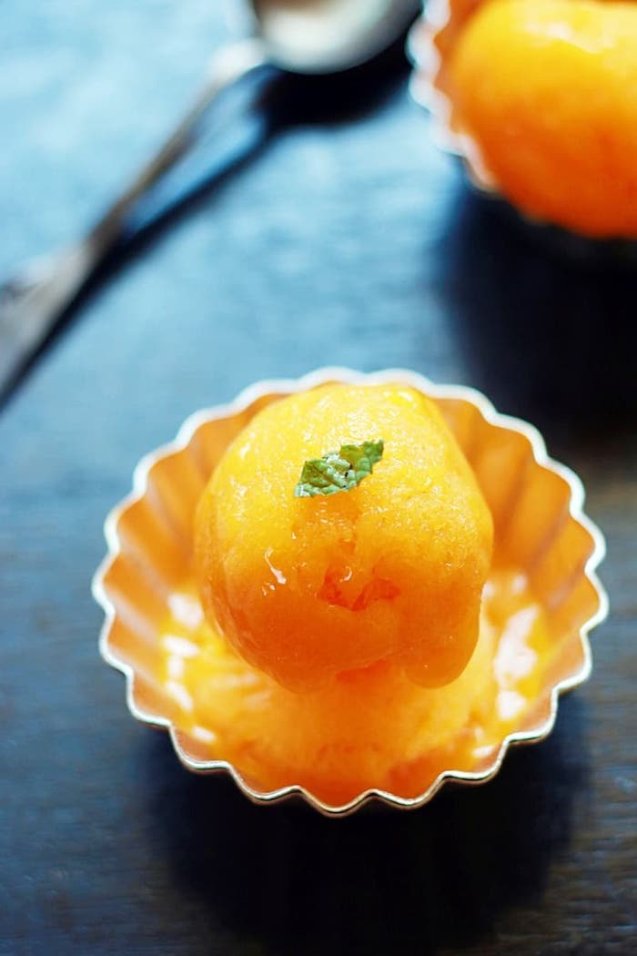 one scoop of mango sorbet inside metal cupcake holder best summer desserts mini mint leaf on top