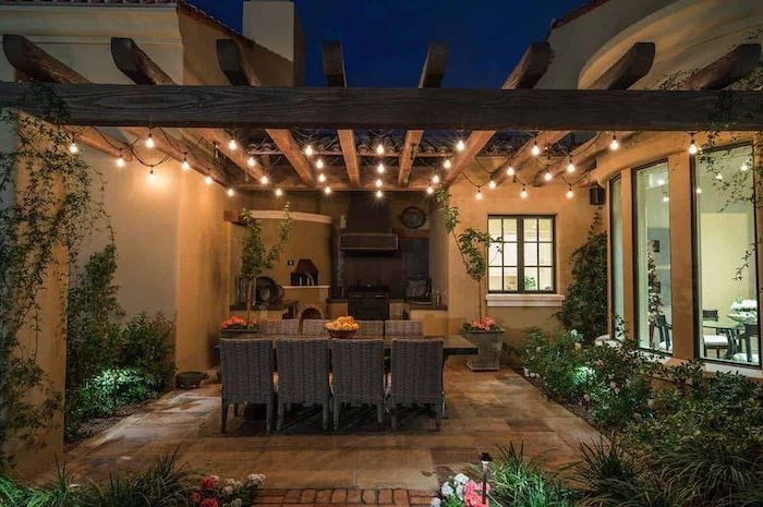 outdoor grill station fireplace and cabinets tiled floor large dining table with eight chairs strings of lights wrapped around wooden beams