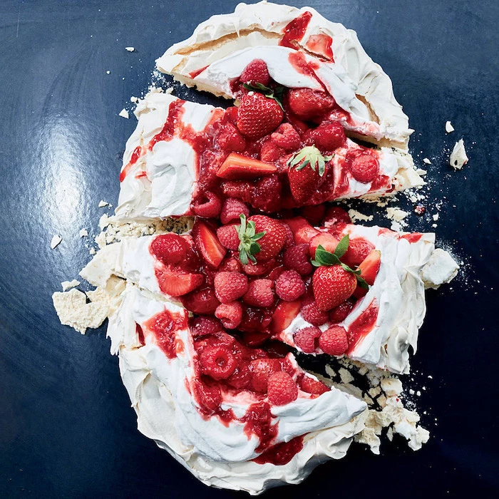 pavlova cake with strawberries on top no bake recipes cut into slices on dark surface