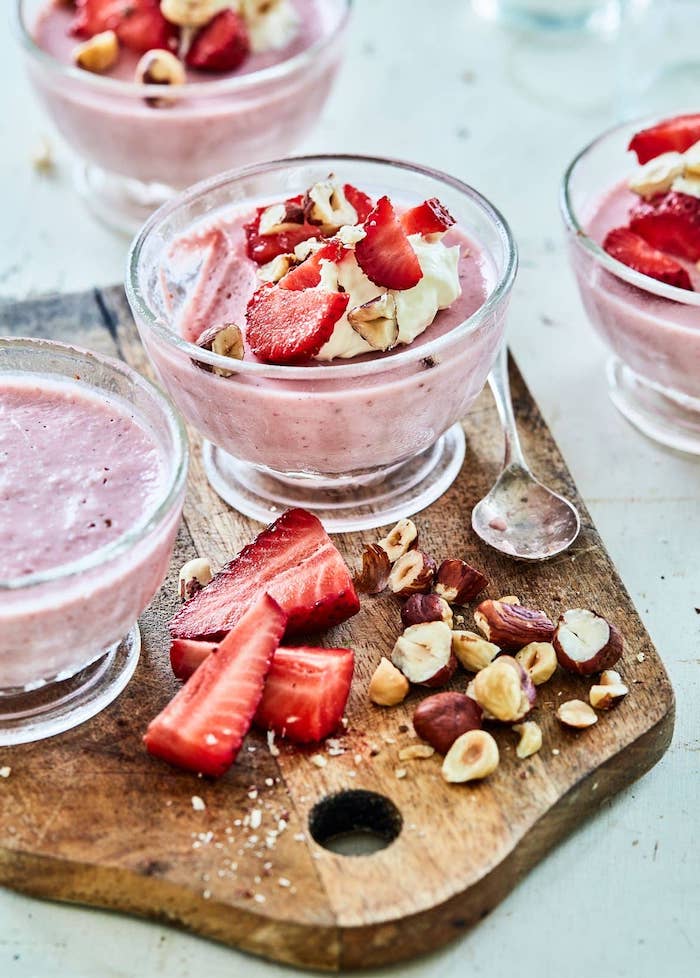 strawberry mousse inside small glasses no bake desserts garnished with crushed hazelnuts and sliced strawberries
