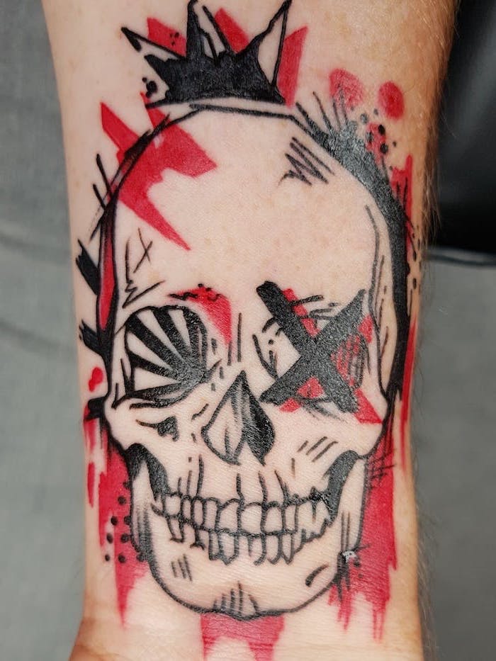 trash polka skull forearm tattoo of skull with x on one eye surrounded by red and black lines