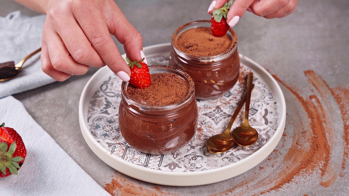 two glass jars with chocolate mousse easy party desserts garnished with cocoa powder and strawberries