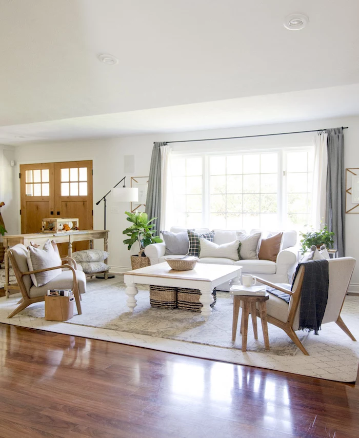 white carpet on wooden floor, industrial farmhouse decor, white sofa with throw pillows, grey armchairs, wooden coffee table