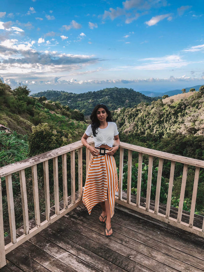 woman wearing white and orange striped skirt white t shirt tied at the waist cute casual summer outfits leaning on balcony