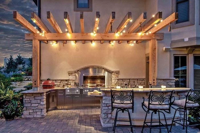 wooden beams with strings of light modern outdoor kitchen grill and metal cabinets kitchen island made of stone black metal bar stools