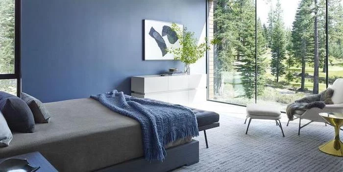 blue accent wall tall windows bedroom wall decor ideas small bed with blue blanket throw pillows floor covered with white carpet