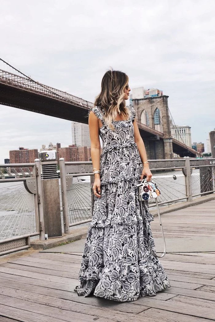 brooklyn bridge in the background flowy dresses brunette woman wearing lonf black and white printed dress standing on the pier