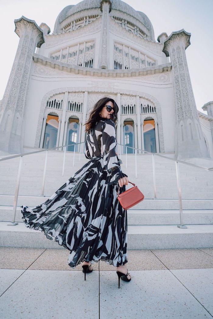 brunette woman wearing long black and white dress summer wedding guest dresses black sandals brown leather bag standing in front of church