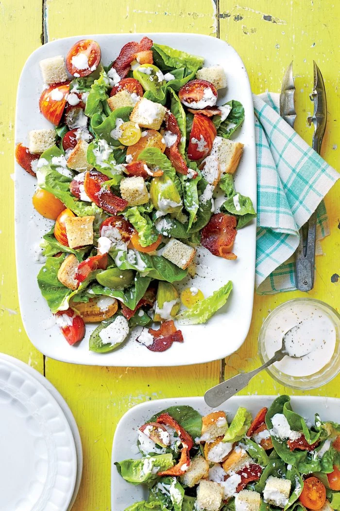 croutons prosciutto halved cherry tomatoes green salad with dressing summer salads white plate on yellow wooden surface