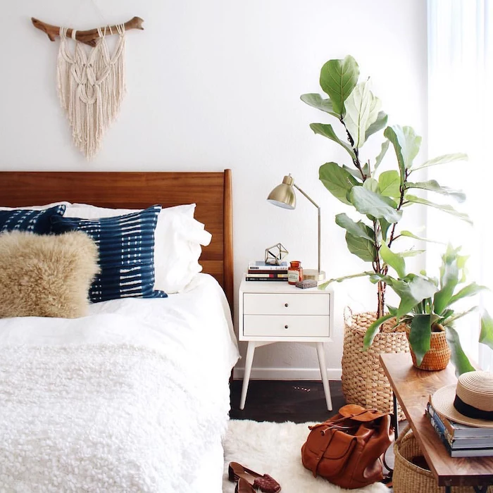 dark wooden floor with white carpet white bed sheets on bed with wooden bed frame blue throw pillows potted plants