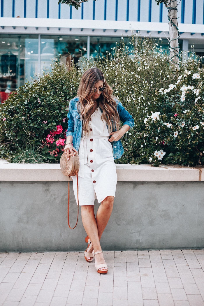 denim jacket on top of white dress worn by woman with long wavy hair cotton summer dresses beige sandals bag sunglasses