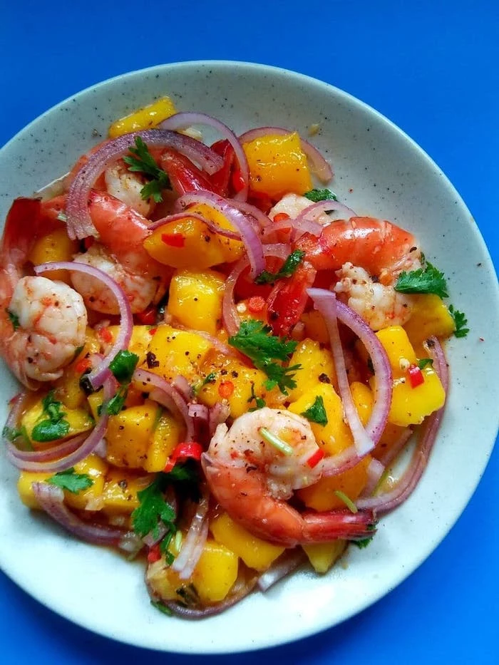 different types of salads mango prawn salad with onion parsley inside white ceramic bowl on blue surface