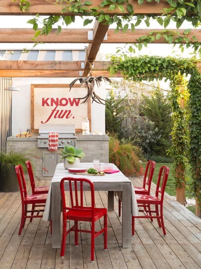 dining wooden table surrounded by red metal chairs next to grill station concrete patio ideas under wooden pergola