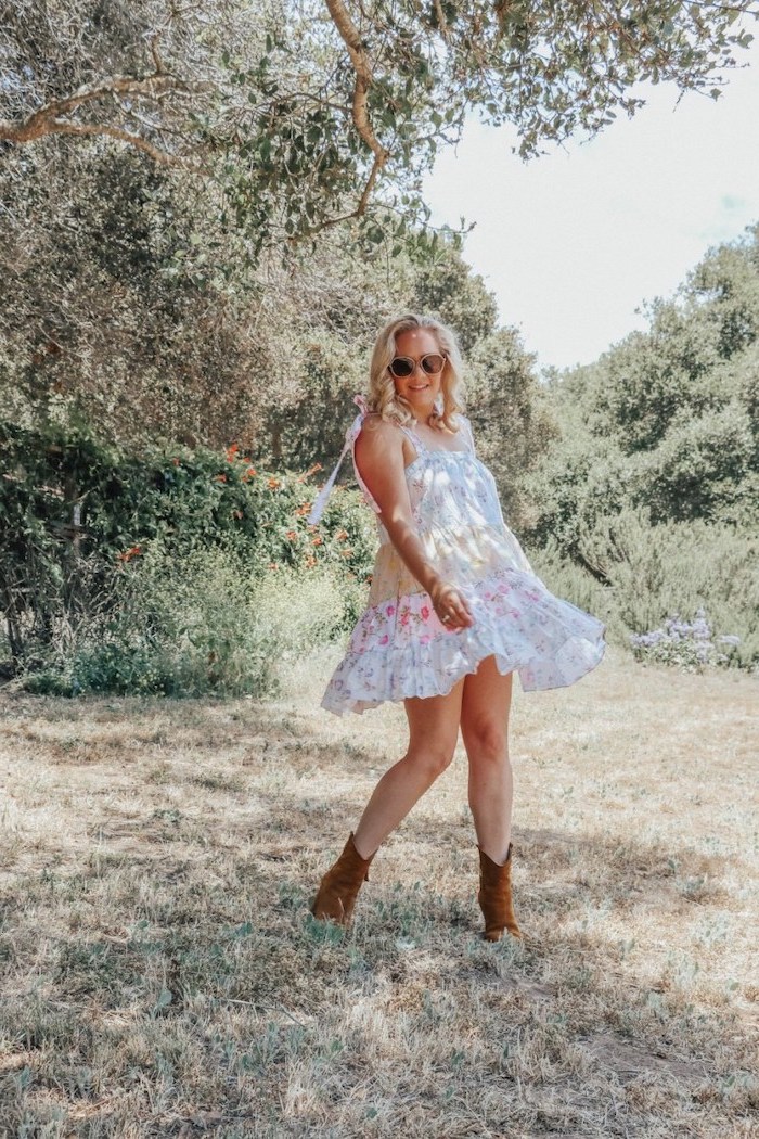 flowy dresses in white with pink flowers worn by woman with medium length blonde wavy hair wearing brown velvet boots