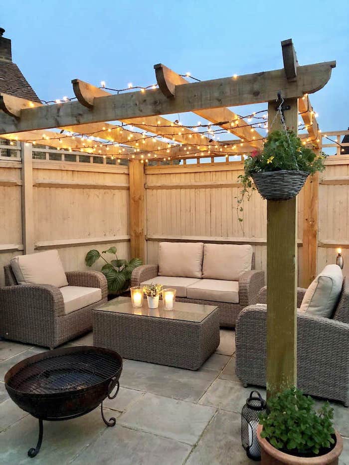garden furniture set with white cushions under wooden pergola with fairy light backyard paver ideas stone tiled floor