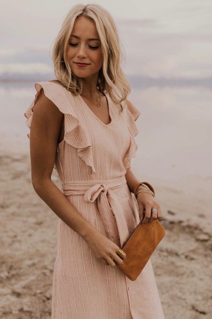 girl standing on the beach with blonde wavy hair cute summer dresses wearing pink dress holding brown velvet purse