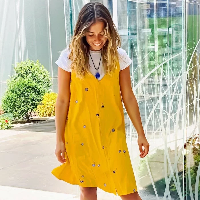 girl with balayage hair wearing white t shirt under yellow dress with blue flowers womens casual summer dresses standing on sidewalk