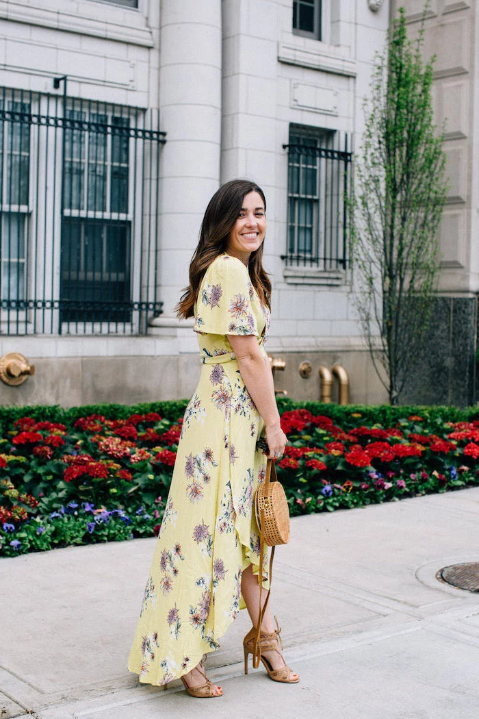 girl with dark brown hair wearing long yellow dress with purple flowers summer wedding guest dresses brown sandals and bag