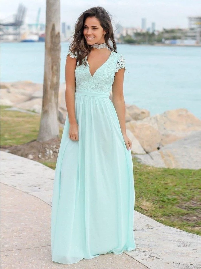 girl with medium length brown wavy hair wearing long blue dress with lace top wedding guest outfits standing on a pier