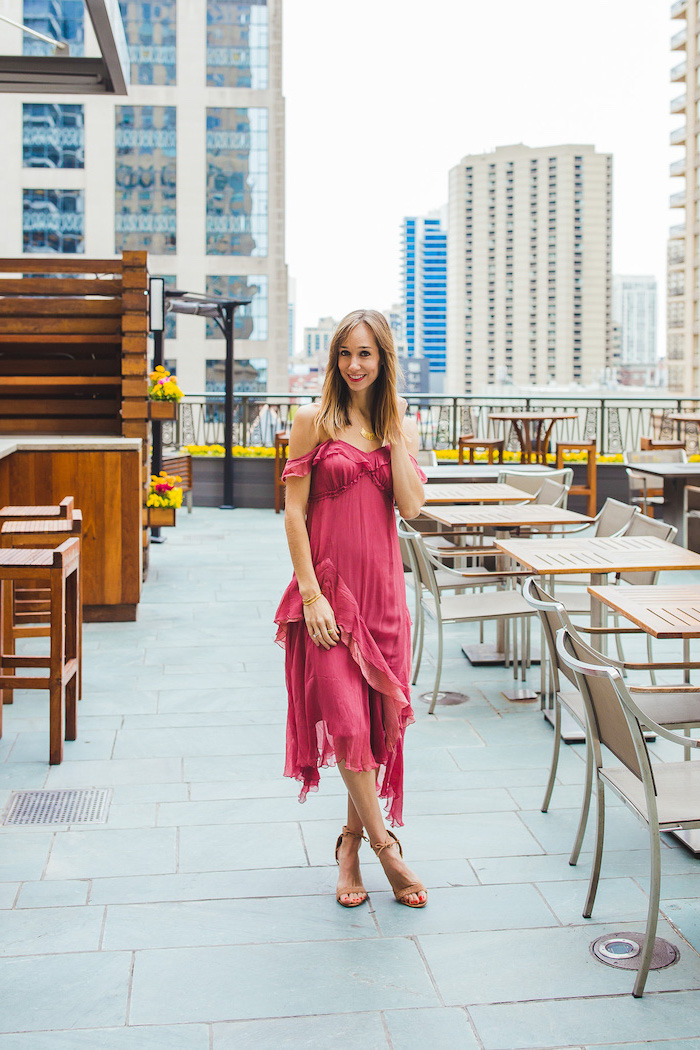 girl with medium length dark blonde hair summer wedding guest dresses wearing dark pink midi dress standing on balcony