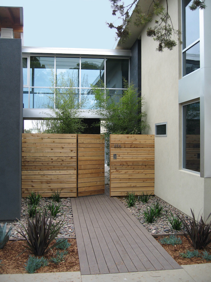 gravel on both sides of wooden pathway simple landscaping ideas leading to wooden gate with bushes planted on both sides