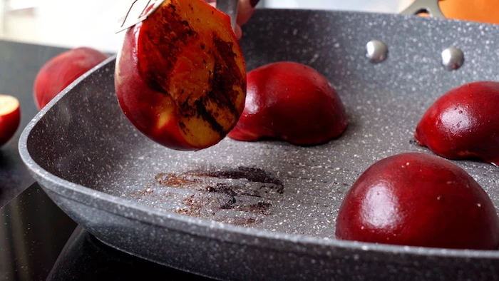 halved peaches being grilled onto a gray grill pan summer salad recipe held with tongs