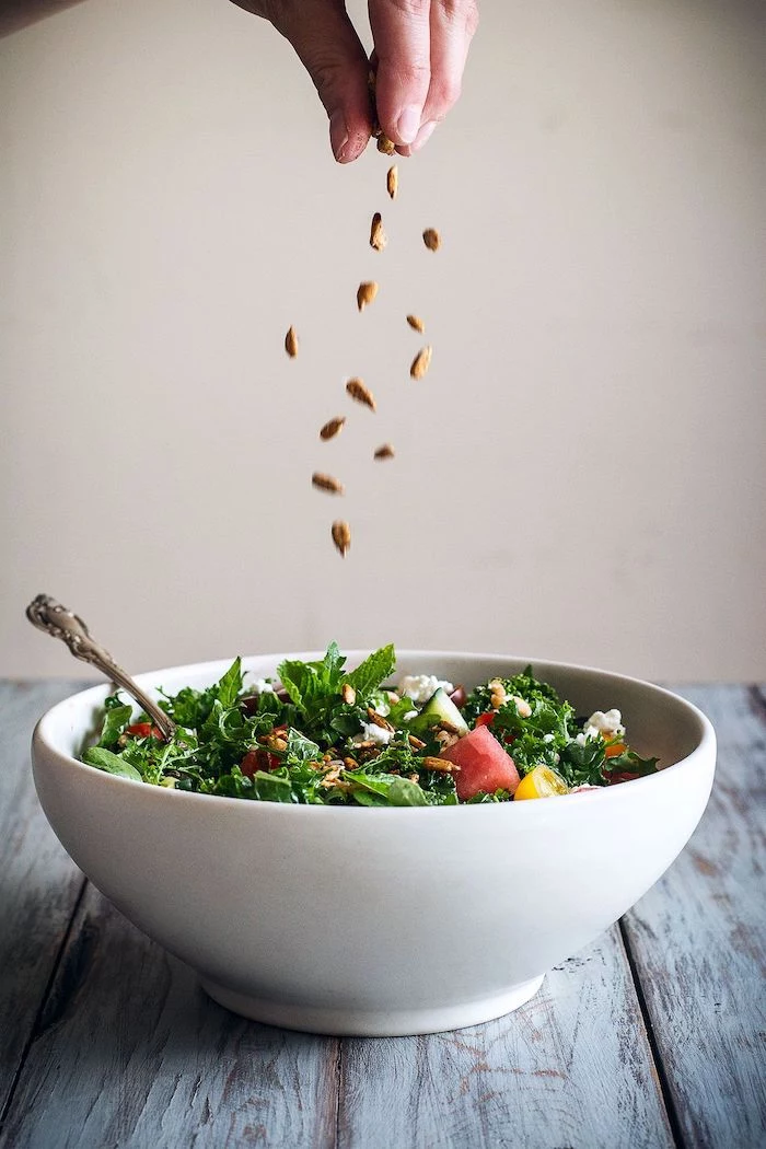 kale salad with watermelon halved cherry tomatoes seeds different types of salads inside white bowl on wooden table