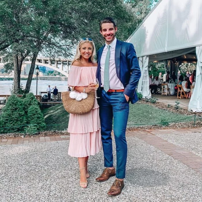 man wearing suit woman wearing pleated strapless pink midi dress elegant dresses for wedding guests standing next to large tent