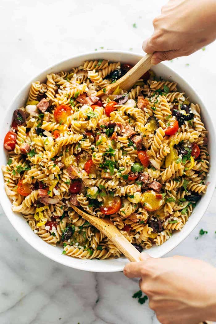 pasta salad with halved cherry tomatoes bacon olives how to make salad italian pasta salad in white bowl two wooden spoons