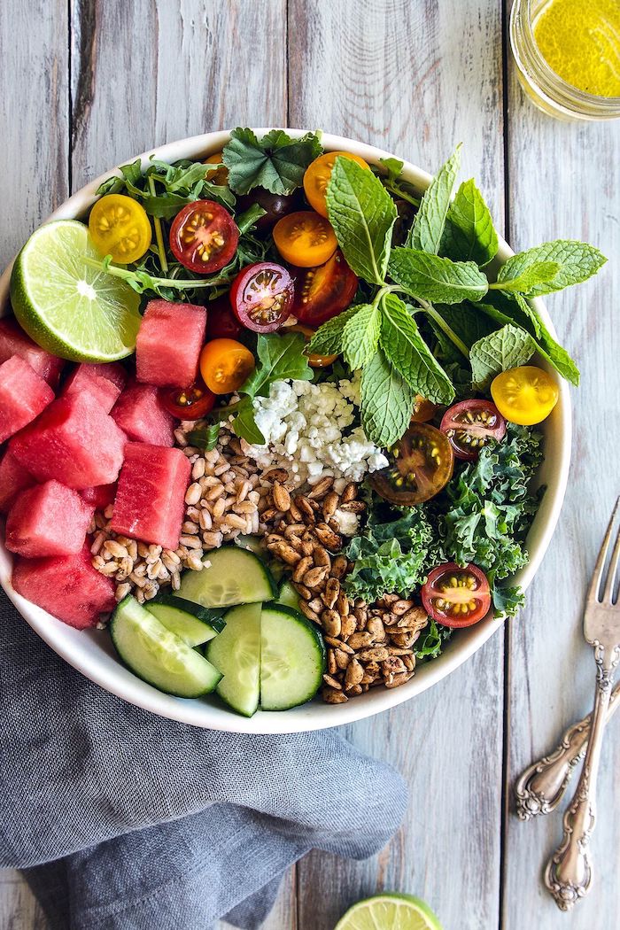 salads for a crowd kale cherry tomatoes cucumbers watermelon mint seeds inside white bowl on wooden table