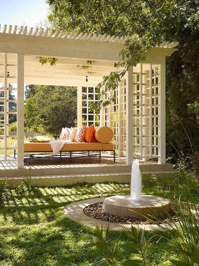 stone patio ideas white woden pergola black metal sofa with orange cushions and throw pillows in the middle of grass field