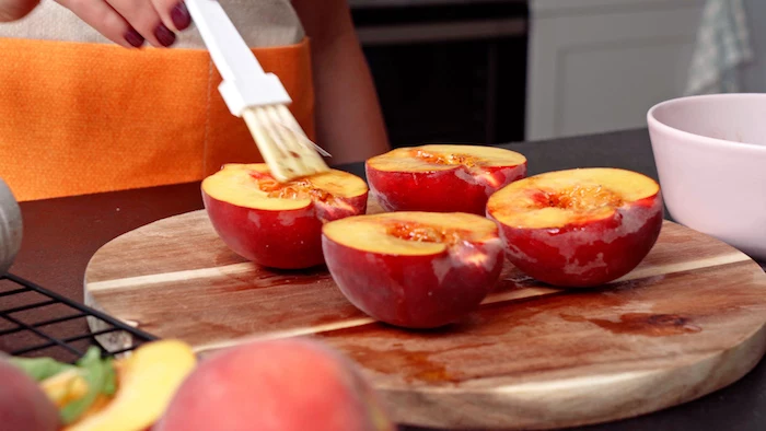 summer salad recipe halved peaches being covered with dressing arranged on wooden cutting board