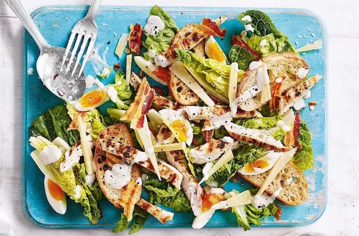 summer salad recipes ceasers salad with chicken strips bacon boiled eggs placed on blue wooden board