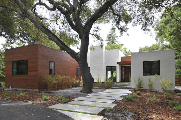 tiled pathway leading to wooden door on one storey modern house front yard landscaping ideas with rocks surrounded by trees and bushes