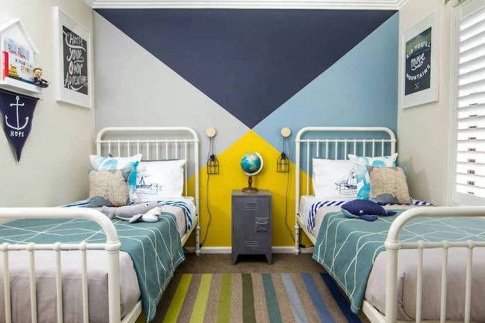 two beds with white metal frames boys bedroom decor geometric accent wall behind them in shades of blue and yellow colorful carpet