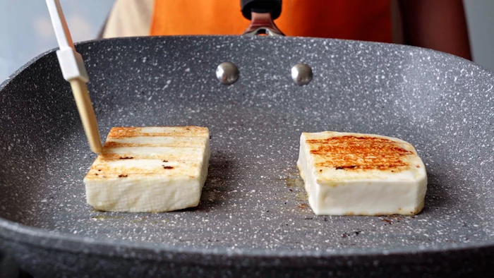two slices of halloumi cheese being grilled onto a gray grill pan summer salad recipe