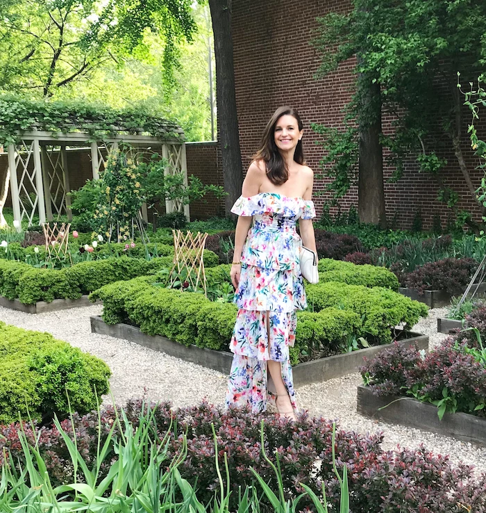 wedding guest dresses brunette woman wearing strapless white dress with green pink blue purple flowers standing in a garden